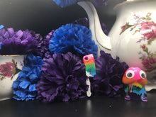 Load image into Gallery viewer, image is a rainbow(pink, red, orange, yellow, green, turquoise, blue, purple) butcher knife earring with a silver handle.  background of image has blue and purple silk flowers (carnations) and a white floral-patterned teapot and teacup. next to the earring is a small rainbow penis with googly eyes. 
