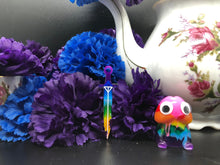 Load image into Gallery viewer, image is a reverse rainbow(pink, red, orange, yellow, green, turquoise, blue, purple from the bottom up) long sword earring with white paint engraving.  background of image has blue and purple silk flowers (carnations) and a white floral-patterned teapot and teacup. next to the earring is a small rainbow penis with googly eyes. 
