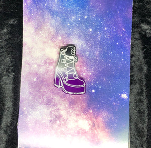 an Asexual Pride (black to grey to white to purple) broomrider boot earring with bright white highlights. In the background is a nebula and a black crushed velvet border.