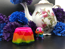 Load image into Gallery viewer, image is a rainbow(pink, red, orange, yellow, green, turquoise, blue, purple) trinket dish.  background of image has blue and purple silk flowers (carnations) and a white floral-patterned teapot and teacup. next to the earring is a small rainbow penis with googly eyes. 
