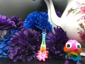 image is a rainbow(pink, red, orange, yellow, green, turquoise, blue, purple) baseball bat with white paint engraving.  background of image has blue and purple silk flowers (carnations) and a white floral-patterned teapot and teacup. next to the earring is a small rainbow penis with googly eyes.