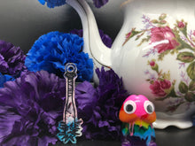 Load image into Gallery viewer, image is a blue, pink, and white baseball bat earring with black paint engraving.  background of image has blue and purple silk flowers (carnations) and a white floral-patterned teapot and teacup. next to the earring is a small rainbow penis with googly eyes.

