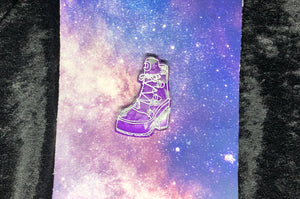 A broomrider boot earring with swirls of purple and grey color and bright white highlights, against a pink-and-blue nebula and black crushed velvet background.