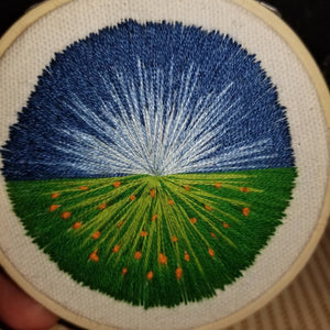 Hand embroidered modern landscape art of a blue sky and green meadow with orange flowers