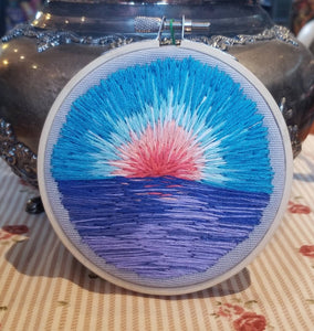Hand embroidered landscape with a sunrise with blue skies above a body of water